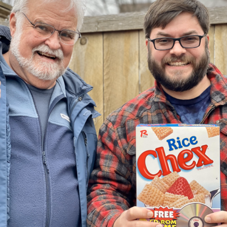 A father and his adult son posing with a box of Rice Chex cereal.